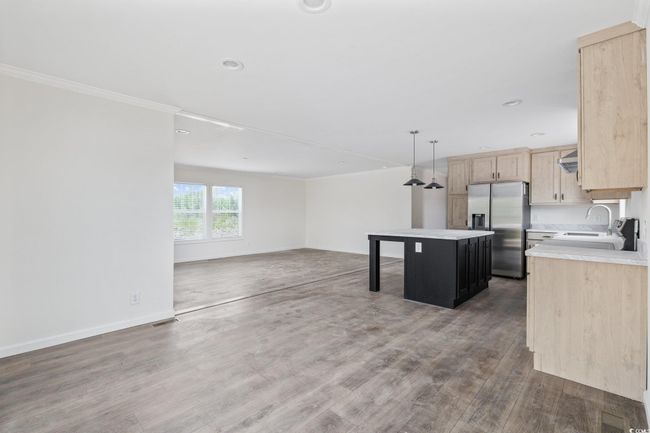 Kitchen featuring stainless steel fridge, light brown cabinetry, ornamental molding, light countertops, and open floor plan | Image 15