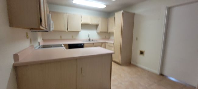 Kitchen with a peninsula, a sink, light countertops, dishwashing machine, and range | Image 7