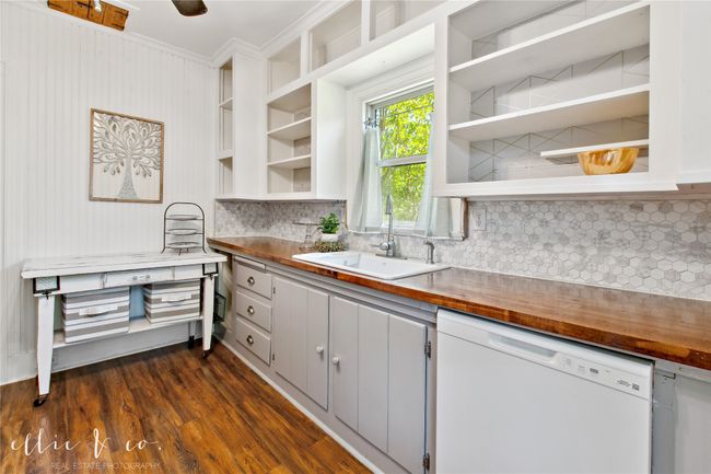 Kitchen featuring white dishwasher, open shelves, a sink, butcher block countertops, and decorative backsplash | Image 16