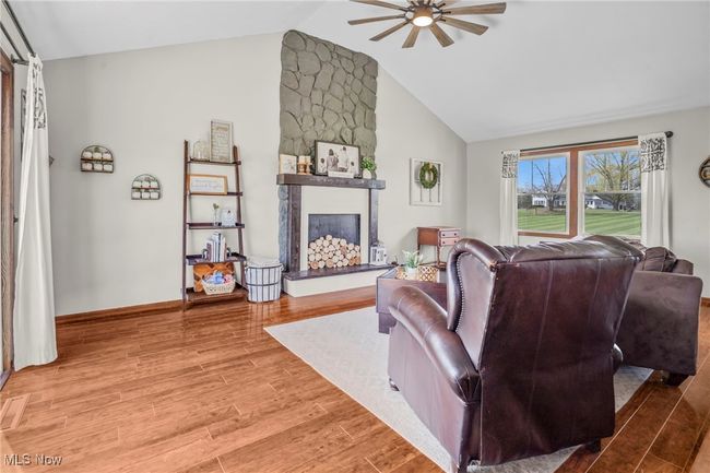 Living room featuring a large fireplace, light wood-style floors, baseboards, a ceiling fan, and high vaulted ceiling | Image 14
