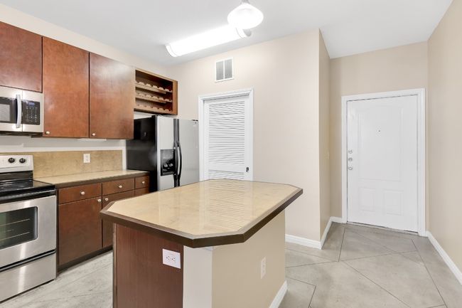 Kitchen featuring light tile patterned floors, visible vents, a center island, stainless steel appliances, and light countertops. All new paint. | Image 4