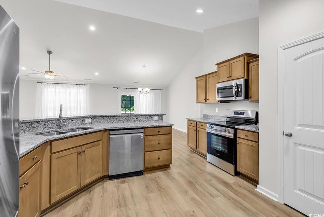 Kitchen featuring appliances with stainless steel finishes, a sink, lofted ceiling, light wood-type flooring, and brown cabinets | Image 12