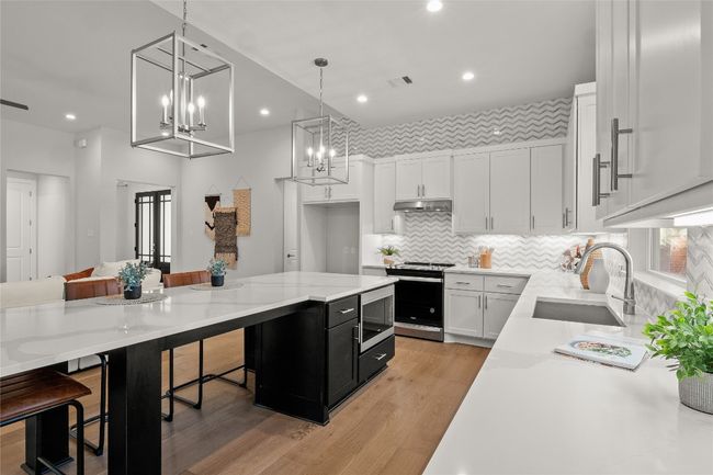 Kitchen with under cabinet range hood, an inviting chandelier, dark cabinets, stainless steel appliances, and a sink | Image 11