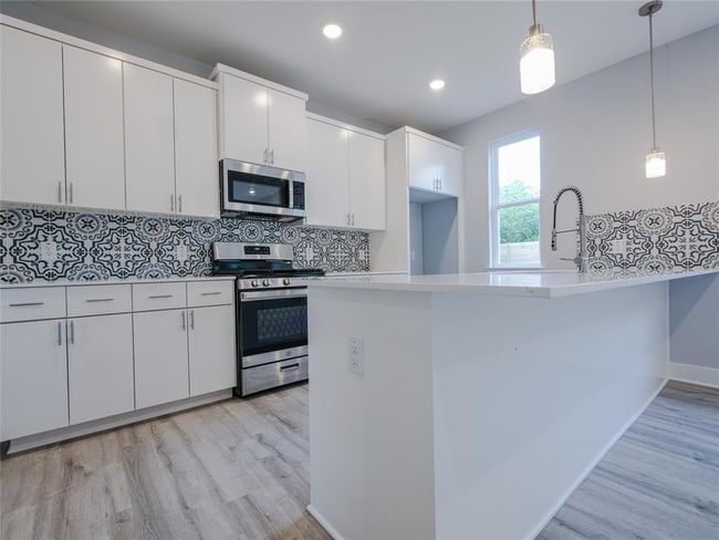 Kitchen featuring appliances with stainless steel finishes, light wood finished floors, tasteful backsplash, white cabinets, and recessed lighting | Image 7