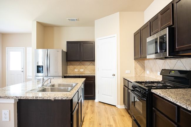Kitchen featuring appliances with stainless steel finishes, a sink, a center island with sink, and dark brown cabinets | Image 8