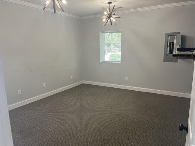 Empty room featuring a chandelier, crown molding, dark colored carpet, and electric panel | Image 6