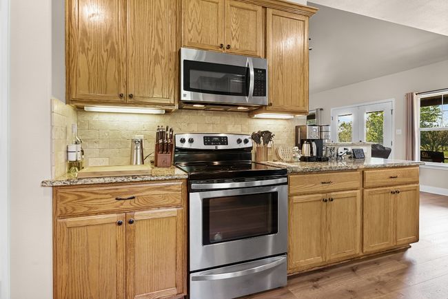 Kitchen with light wood-style floors, light stone countertops, a peninsula, stainless steel appliances, and decorative backsplash | Image 12