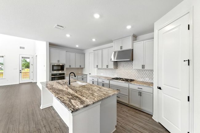 Kitchen with under cabinet range hood, a sink, stainless steel appliances, decorative backsplash, and a center island with sink | Image 12