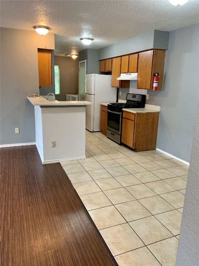 Kitchen featuring light countertops, gas stove, under cabinet range hood, brown cabinetry, and freestanding refrigerator | Image 5