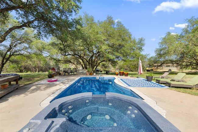 View of swimming pool with a patio area, a pool with connected hot tub, and view of scattered trees | Image 9