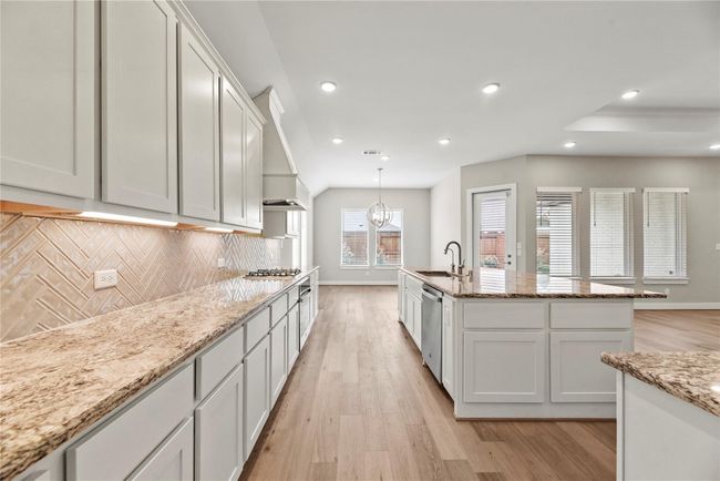 This bright and open kitchen offers expansive prep space, extensive cabinetry, and elegant finishes including granite countertops and herringbone tile backsplash. The layout flows seamlessly into the dining area and family room, making it perfect for entertaining or enjoying everyday moments at home. | Image 21