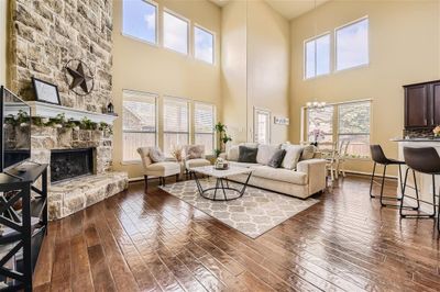 Living room featuring a stone fireplace, a high ceiling, dark hardwood / wood-style flooring, and a notable chandelier | Image 3