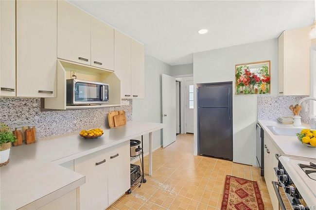 Kitchen featuring stainless steel appliances, backsplash, sink, light tile patterned flooring, and white cabinets | Image 4