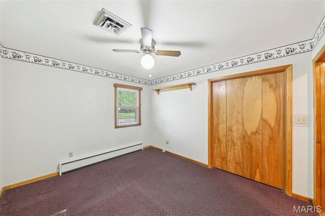 Unfurnished bedroom featuring a baseboard radiator, dark colored carpet, a closet, and ceiling fan | Image 20