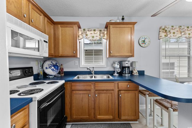 Kitchen featuring range with electric stovetop, white microwave, a sink, brown cabinets, and a peninsula | Image 11