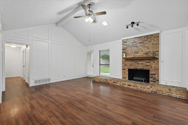 Unfurnished living room featuring dark wood finished floors, ceiling fan, a textured ceiling, a decorative wall, and a fireplace | Image 5