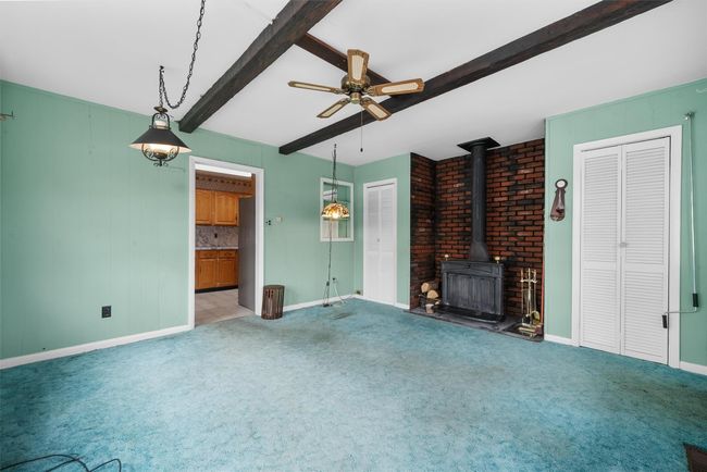 Unfurnished living room featuring carpet floors, a wood stove, beamed ceiling, and ceiling fan | Image 18