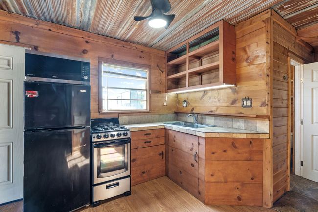 Kitchen featuring freestanding refrigerator, stainless steel gas range, a sink, a ceiling fan, and brown cabinetry | Image 17