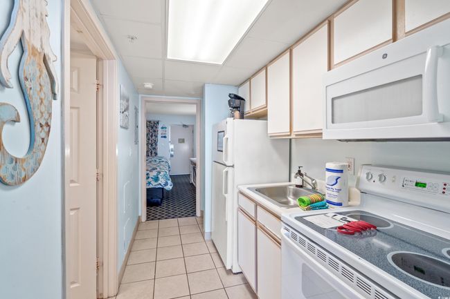 Kitchen featuring white appliances, light countertops, light tile patterned flooring, and white cabinetry | Image 12