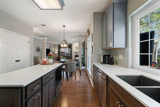 Kitchen with light countertops, stainless steel dishwasher, dark wood-style floors, open floor plan, and decorative backsplash | Image 11
