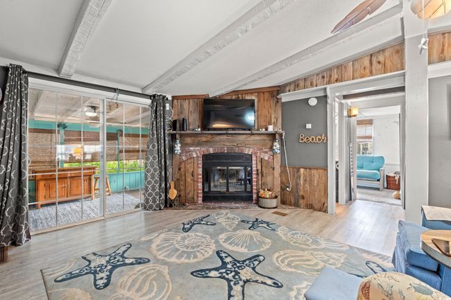 Living room featuring a brick fireplace, wood walls, vaulted ceiling with beams, and hardwood / wood-style flooring | Image 4