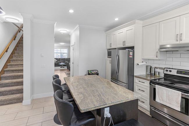 Kitchen featuring stainless steel appliances, under cabinet range hood, light stone countertops, ornamental molding, and decorative backsplash | Image 9