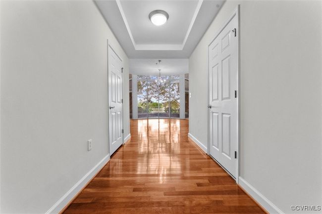Hallway featuring baseboards, light wood-style flooring, a tray ceiling, and a notable chandelier | Image 21
