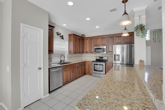 Kitchen featuring appliances with stainless steel finishes, light stone counters, a sink, and decorative light fixtures | Image 13