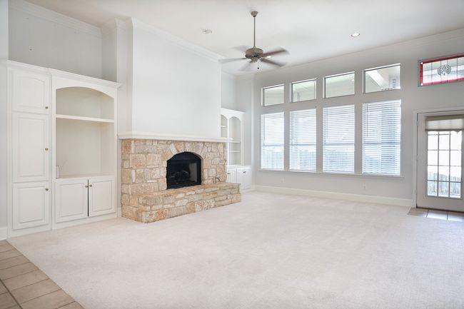 Unfurnished living room featuring built in shelves, ceiling fan, carpet, a fireplace, and crown molding | Image 6