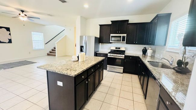 Kitchen featuring appliances with stainless steel finishes, light tile patterned flooring, tasteful backsplash, open floor plan, and a kitchen island | Image 18