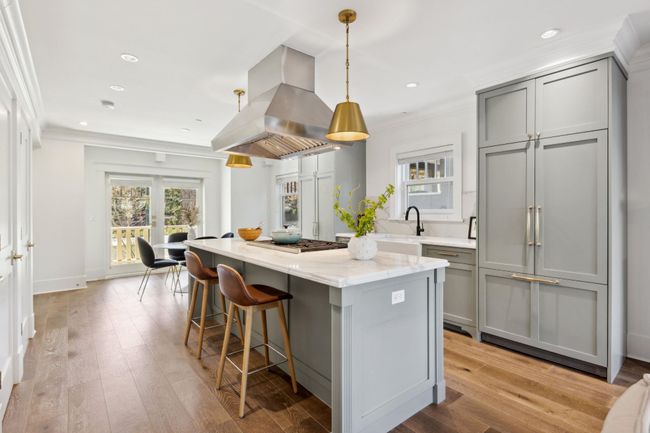 Kitchen featuring a kitchen bar, island range hood, gray cabinets, light stone countertops, and a kitchen island | Image 10