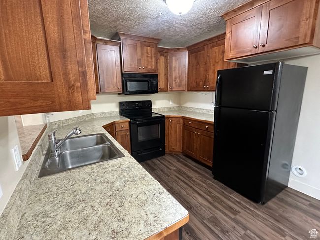 Kitchen with a textured ceiling, dark wood-style flooring, a sink, light countertops, and black appliances | Image 9