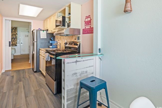 Kitchen featuring stainless steel appliances, dark wood-type flooring, decorative backsplash, ventilation hood, and open shelves | Image 11
