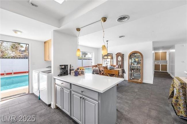 Kitchen with separate washer and dryer, a peninsula, light countertops, and dark tile patterned floors | Image 8