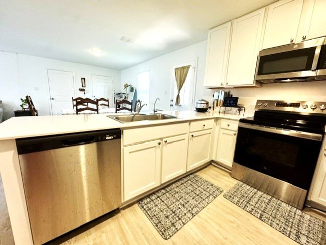 Kitchen with stainless steel appliances, light wood-style floors, a peninsula, light countertops, and white cabinetry | Image 7