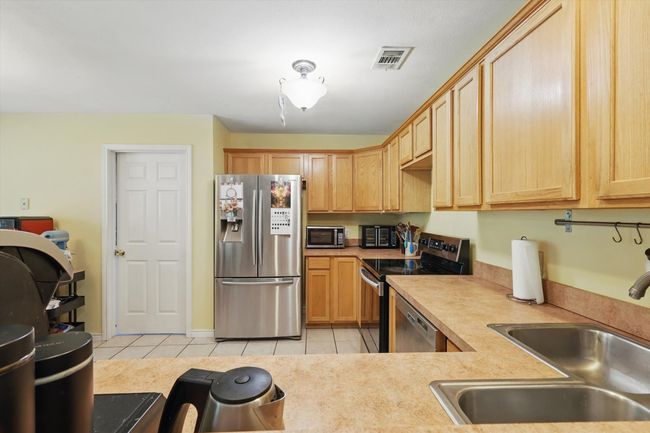 Kitchen with light tile patterned floors, visible vents, a sink, light countertops, and stainless steel appliances | Image 13