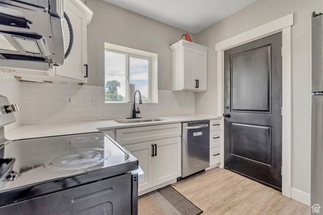 Kitchen with stainless steel dishwasher, electric stove, white microwave, tasteful backsplash, and white cabinetry | Image 8