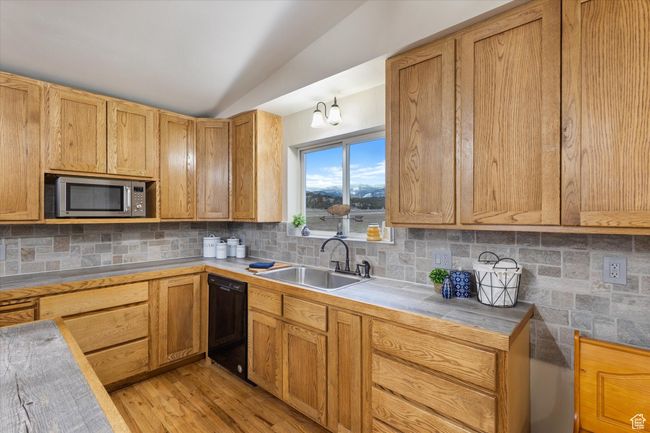 Kitchen with stainless steel microwave, backsplash, dishwasher, lofted ceiling, and a sink | Image 9