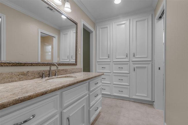 This primary suite bathroom features a spacious vanity with a granite countertop and an elegant framed mirror. Ample white cabinetry provides generous storage, and the neutral tones create a clean, bright atmosphere. | Image 26