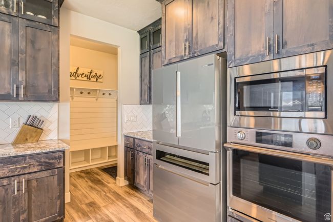 Kitchen with stainless steel appliances, light stone counters, light wood finished floors, and backsplash | Image 9