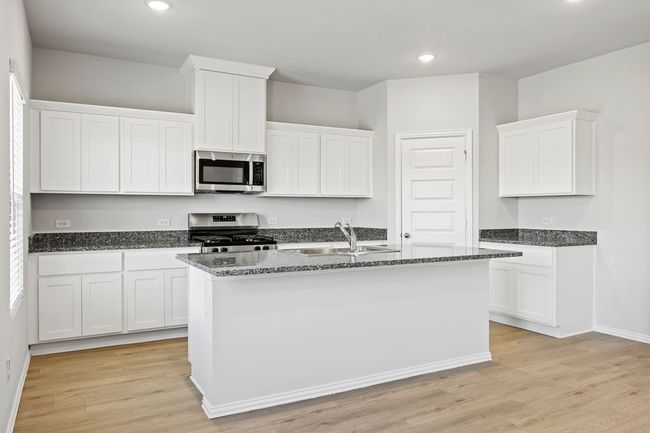Kitchen featuring stainless steel appliances, recessed lighting, dark stone counters, a center island with sink, and light wood finished floors | Image 10