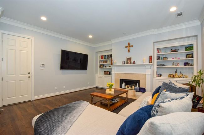 Generous sized, well-lit family room featuring hardwood floors, a fireplace with a white mantel, built-in shelving. The room is finished with crown molding and has a neutral color scheme, offering a comfortable and inviting space | Image 9