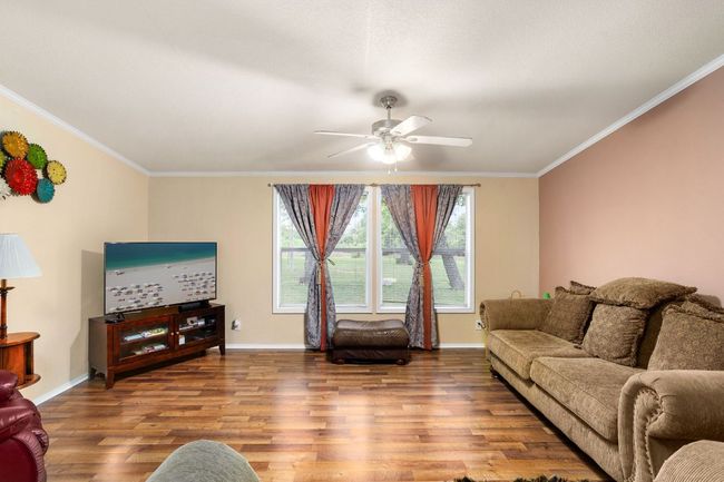 Living area with a ceiling fan, ornamental molding, baseboards, and wood finished vinyl floors | Image 20
