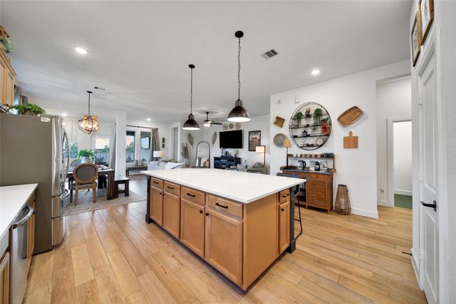 This spacious, open-concept kitchen and living area features hardwood floors, a large island with pendant lighting, and ample natural light. The kitchen includes stainless steel appliances and flows seamlessly into a cozy dining and living space, perfect for entertaining. | Image 22