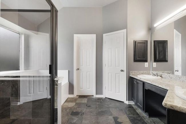 This bathroom features a modern design with slate tile flooring, a double vanity with granite countertops, and a spacious shower. The neutral color palette and ample natural light create a bright and inviting atmosphere. | Image 14