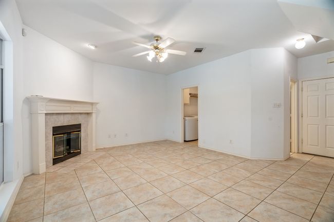 Unfurnished living room with a ceiling fan, light tile patterned flooring, washer / dryer, visible vents, and a tile fireplace | Image 17