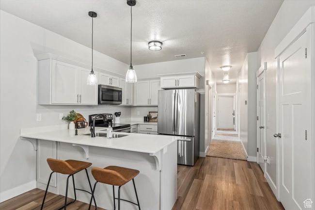 Kitchen featuring appliances with stainless steel finishes, decorative light fixtures, a breakfast bar area, dark wood-style flooring, and a textured ceiling | Image 4