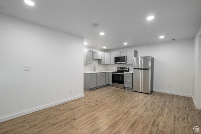 Basement kitchen featuring light wood-style floors, recessed lighting, light countertops, stainless steel appliances, and gray cabinetry | Image 27