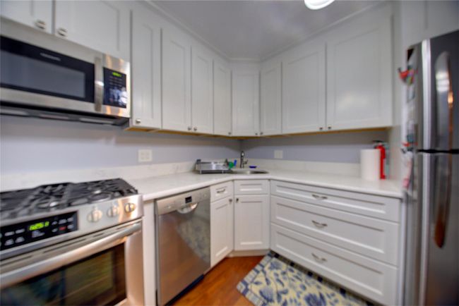 Kitchen with appliances with stainless steel finishes, light countertops, white cabinetry, and wood finished floors | Image 7