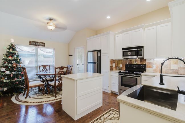Kitchen with white cabinetry, dark wood-type flooring, vaulted ceiling, a kitchen island, and appliances with stainless steel finishes | Image 5